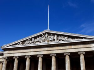 The image showcases the neoclassical facade of one of the Top 10 Museums, featuring twelve Corinthian columns supporting a triangular pediment. Adorned with sculptures in various poses, this architectural marvel is set against a clear blue sky.